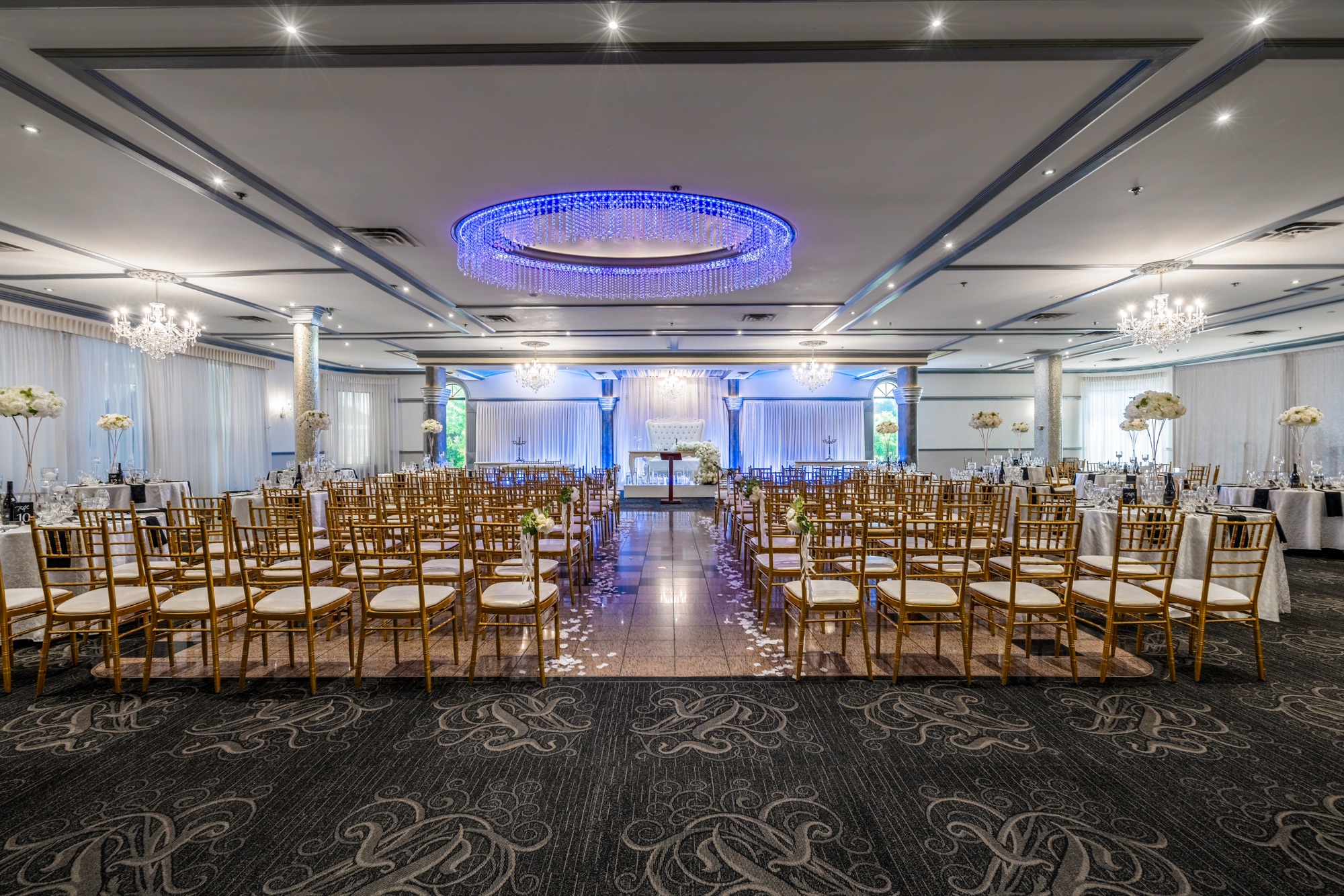 Rows of gold chairs framed by round tables and flowers